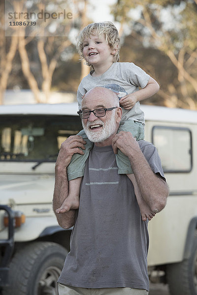 Glücklicher Großvater trägt den Jungen auf den Schultern im Freien.