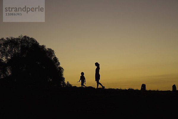 Silhouette Junge und Frau  die bei Sonnenuntergang auf dem Feld gegen den klaren Himmel laufen.