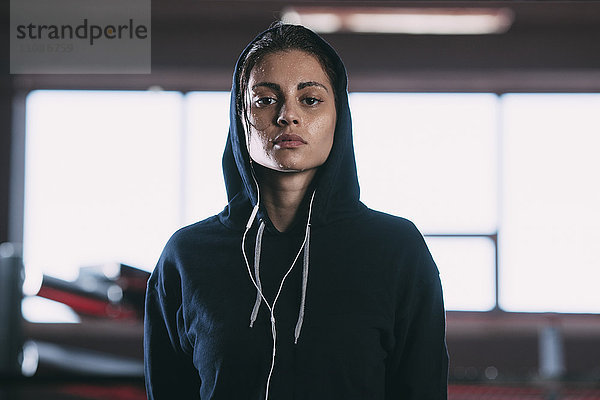 Porträt einer müden Frau in Kapuzenshirt stehend im Fitnessstudio
