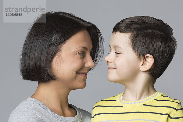 Lächelnde Mutter schaut den Sohn vor grauem Hintergrund an.