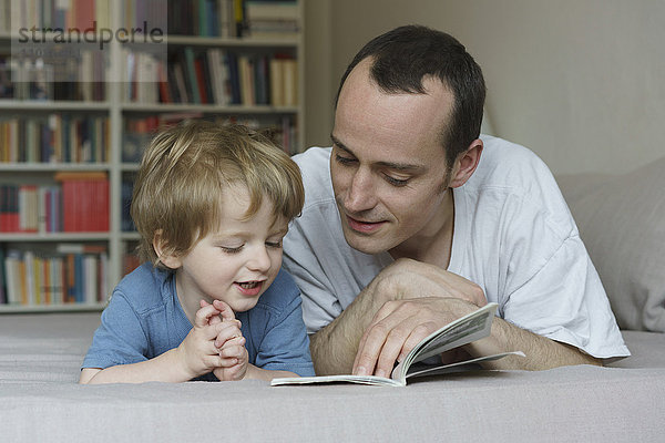 Vater und Sohn lesen Buch  während sie zu Hause im Bett liegen.