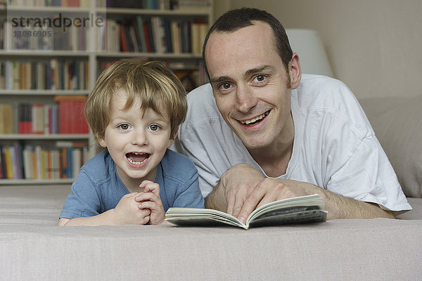 Porträt von lächelndem Vater und Sohn auf dem Bett liegend mit Buch zu Hause