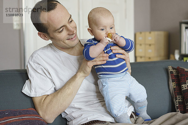 Vater trägt Kleinkind und sitzt zu Hause auf dem Sofa