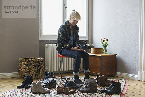 Fröhliche Frau hält Schuhe  während sie zu Hause sitzt.