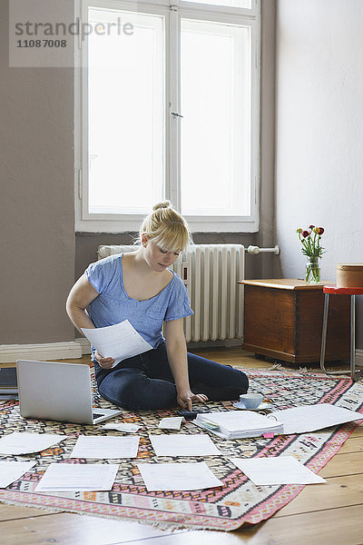 Frau macht Papierkram  während sie zu Hause auf dem Teppich sitzt.