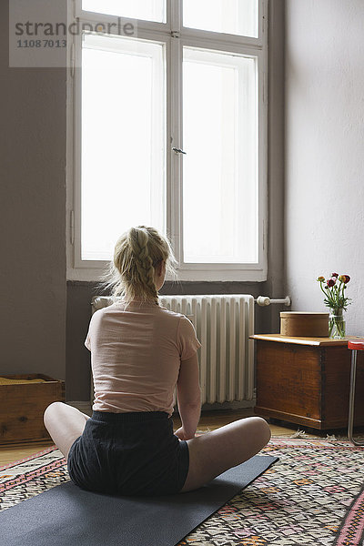 Rückansicht der Frau beim Yoga im Wohnzimmer