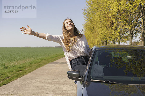 Fröhliche Frau auf dem Autofenster am Straßenrand sitzend