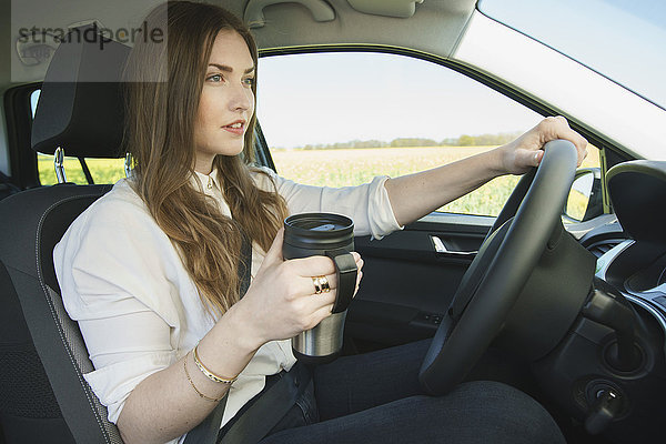 Geschäftsfrau mit isoliertem Getränkebehälter beim Autofahren