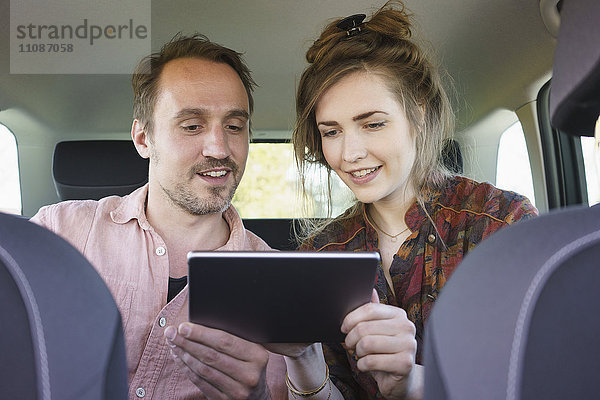 Glückliches Paar mit digitalem Tablett auf Reisen im Auto