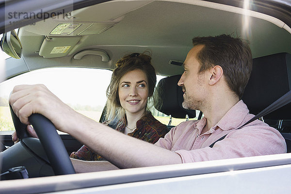 Lächelndes Paar  das sich beim Autofahren ansieht.