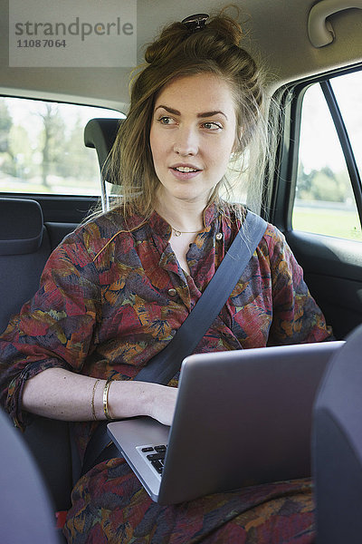 Nachdenkliche junge Frau mit Laptop im Auto