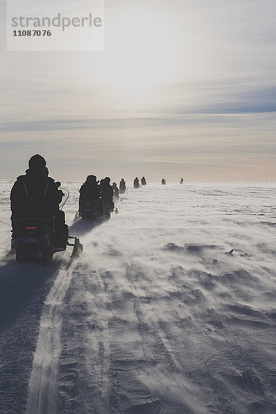 Rückansicht von Schneemobilfahrern gegen den Himmel an einem sonnigen Tag