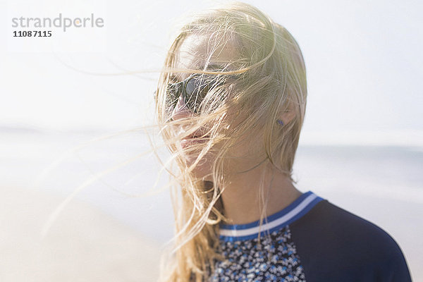 Fröhliche junge Frau mit windgepeitschten Haaren am Strand