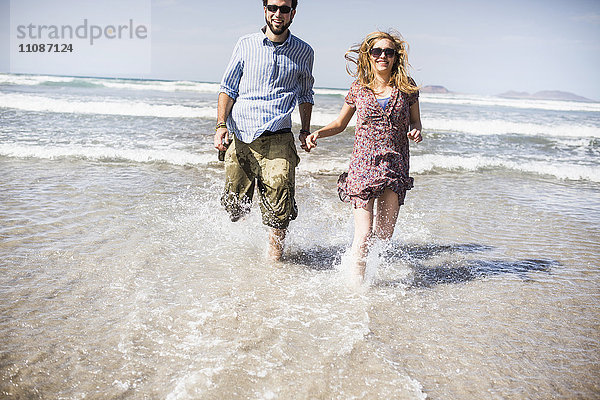 Fröhliches Paar  das an einem sonnigen Tag im Meer läuft