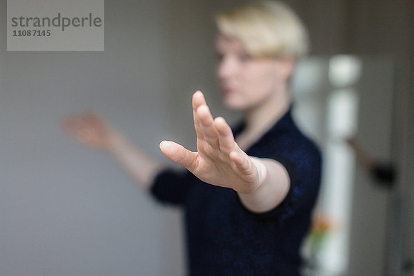 Mittlere erwachsene Frau  die zu Hause mit ausgestreckten Armen trainiert.