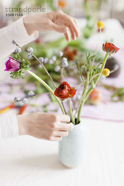 Abgeschnittenes Bild einer Frau  die Blumen in einer Vase auf dem Tisch zu Hause anordnet.