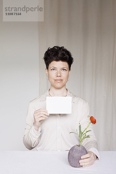 Porträt einer mittleren erwachsenen Frau mit leerer Karte und Blumenvase am Tisch