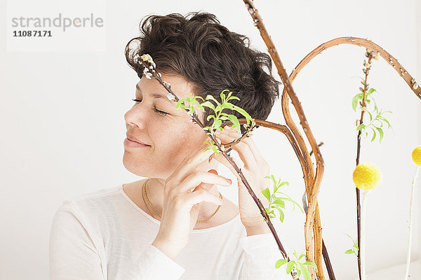Fröhliche mittlere erwachsene Frau fühlt Pflanze vor weißem Hintergrund