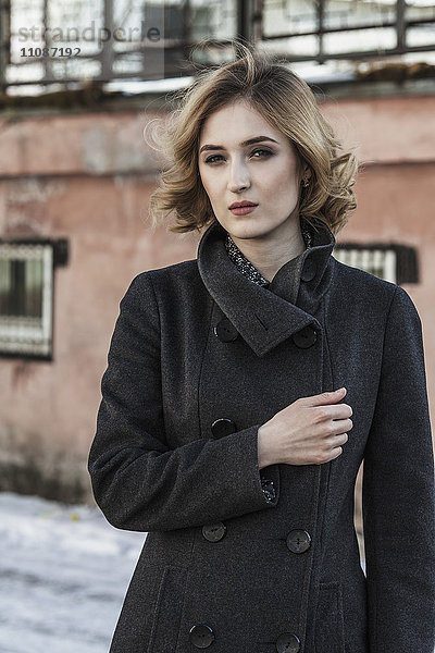 Porträt einer selbstbewussten jungen Frau mit langem Mantel im Freien