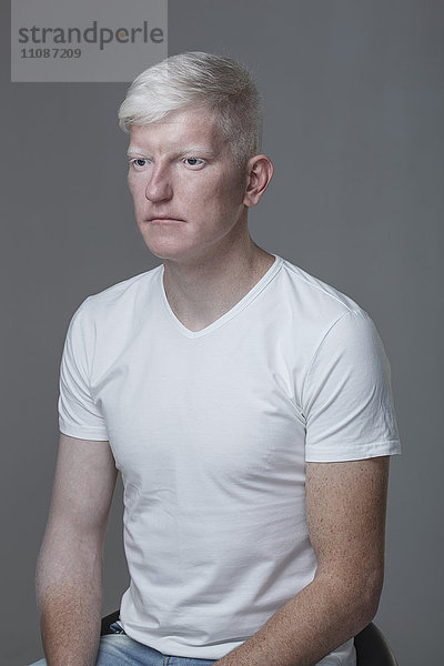Junger Albino-Mann sitzt vor grauem Hintergrund