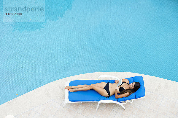 Junge Frau mit Tablette beim Entspannen auf der Lounge am Poolrand