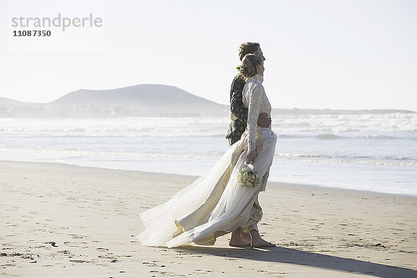 Durchgehende Seitenansicht von Braut und Bräutigam am Strand