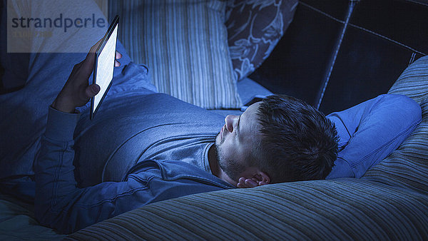 Mann mit digitalem Tablett beim Entspannen auf dem Sofa zu Hause