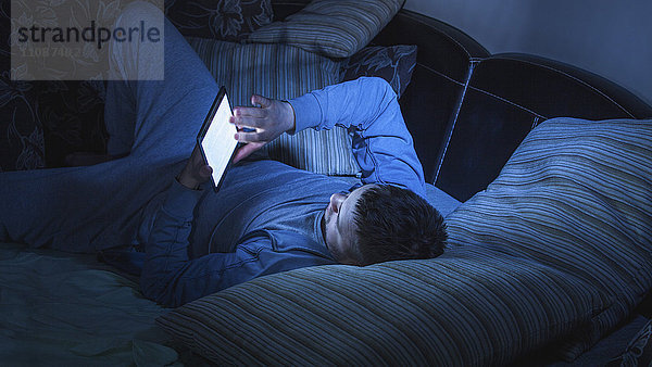 Mann surft im Internet auf einem digitalen Tablett  während er sich zu Hause auf dem Sofa ausruht.