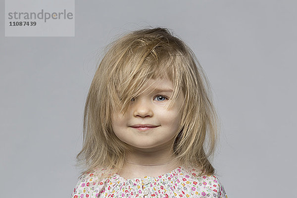 Porträt eines lächelnden Mädchens mit zerzaustem Haar vor grauem Hintergrund