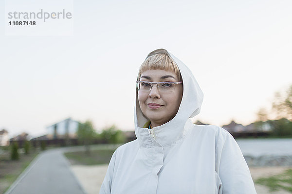 Porträt einer lächelnden Frau mit Kapuze im Park vor klarem Himmel
