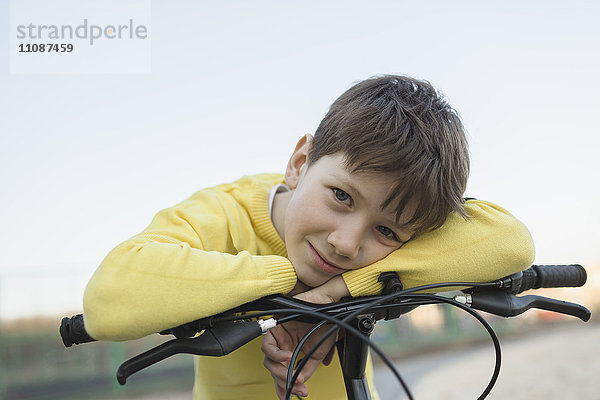 Porträt eines lächelnden Jungen  der sich auf dem Fahrrad gegen den klaren Himmel lehnt.