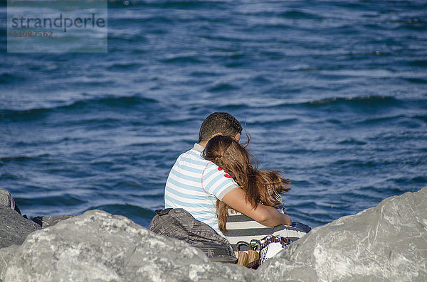 Rückansicht des Paares beim Sitzen am felsigen Meeresufer