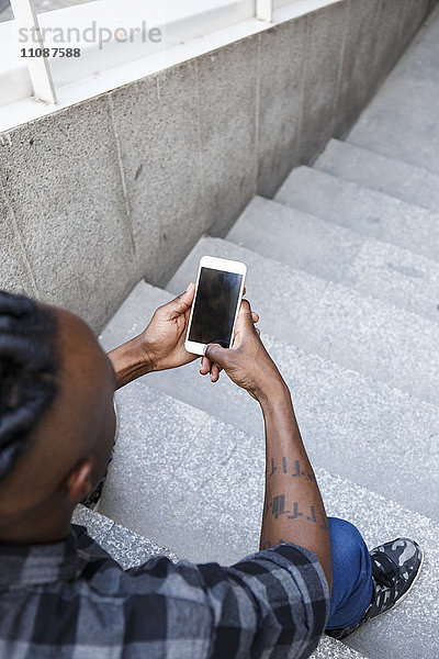 Junger Mann sitzt auf einer Treppe und benutzt ein Smartphone.