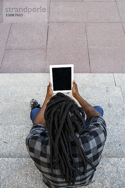 Junger Mann auf der Treppe sitzend  mit Hilfe eines digitalen Tabletts