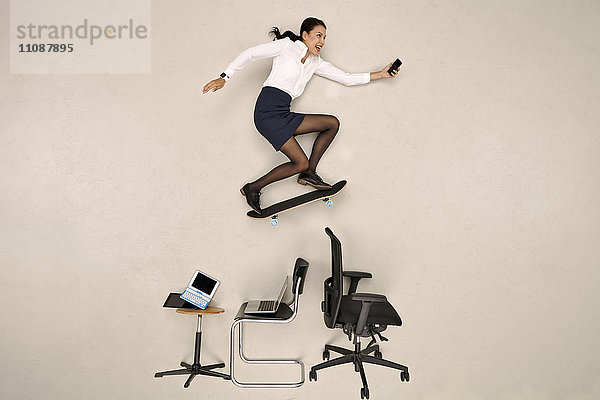 Geschäftsfrau skateboarden über Bürostühle mit Smartphone