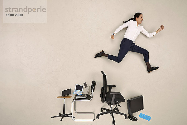 Geschäftsfrau springt über Stühle und Geräte