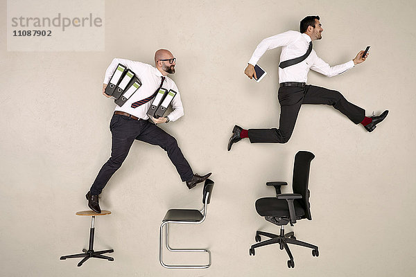 Geschäftsleute  die über Stühle springen  die Ordner und Geräte tragen.
