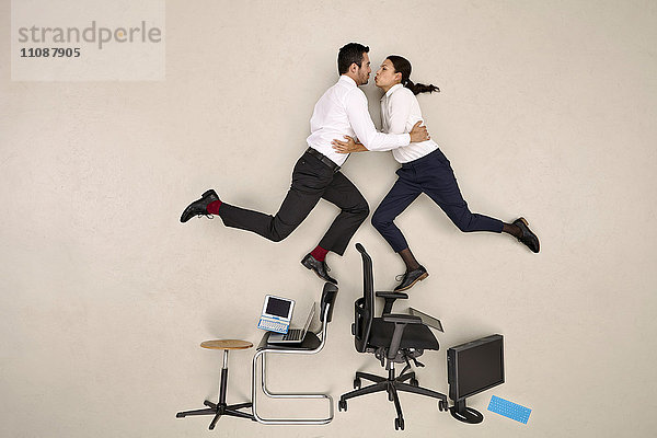 Zwei Kollegen balancieren auf Stühlen und Küssen
