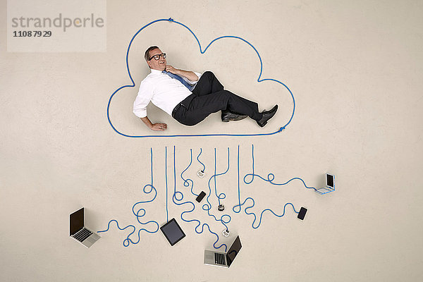 Geschäftsmann liegt in einer Wolke  die mit mobilen Geräten verbunden ist.