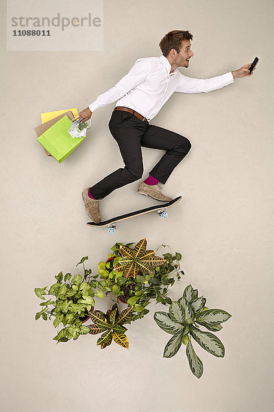 Skateboarding Geschäftsmann in der Natur mit Einkaufstaschen und Smartphone