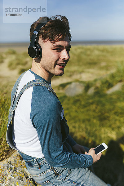 Entspannter junger Mann beim Musikhören mit kabellosen Kopfhörern in der Natur