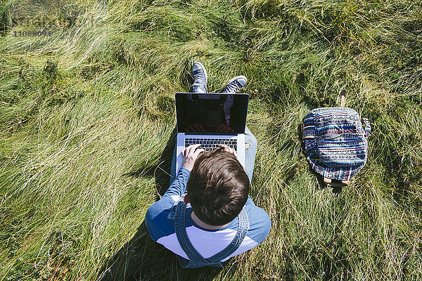 Draufsicht eines jungen Mannes auf einer Wiese mit Laptop