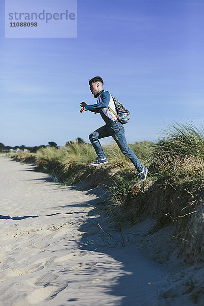 Junger Mann  der am Strand in die Luft springt.