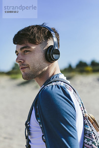 Junger Mann mit kabellosen Kopfhörern am Strand