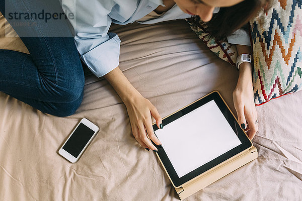 Junge Frau mit digitalem Tablett im Bett  Smartphone