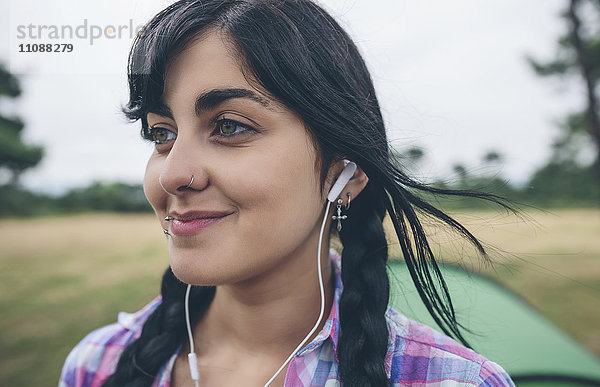 Porträt einer lächelnden jungen Frau mit Piercings beim Musikhören mit Kopfhörern