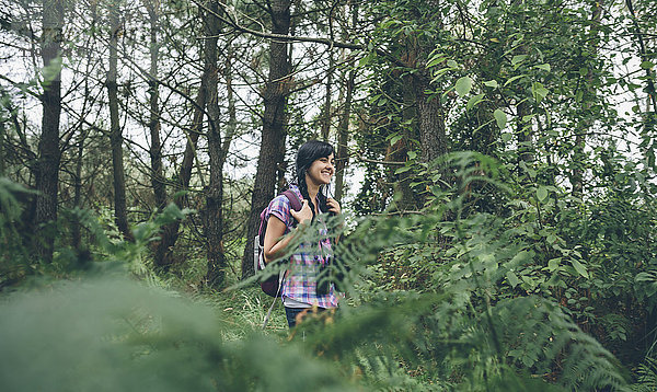 Lächelnde junge Frau mit Rucksack beim Waldspaziergang
