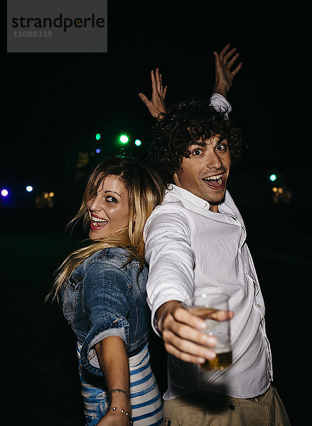Fröhliches junges Paar tanzt Rücken an Rücken beim Sommernachtsfest