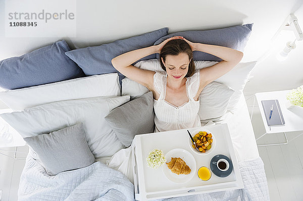 Frau im Bett sitzend mit Frühstückstablett