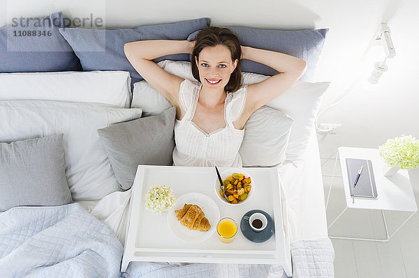 Frau im Bett sitzend mit Frühstückstablett
